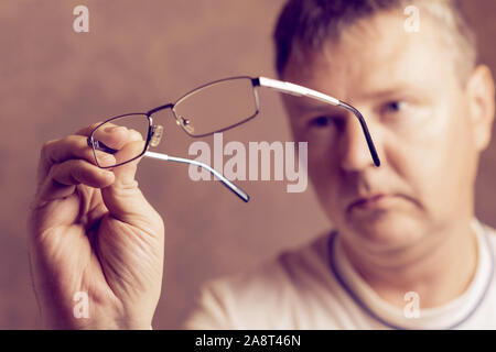 Porträt einer müde Mann mit Brille in den Händen. Mann sieht durch die Brille. Weißer Mann und Brillen in Händen. Selektiver Fokus Stockfoto