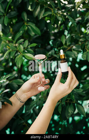 Kleine Flasche verjüngende Wesen und Quarz Massage Roller in die Hände der Kosmetologin Stockfoto