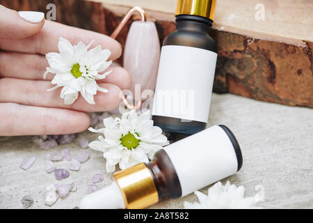 Die Hand der Frau in kleinen Flaschen mit Daisy-Serum mit leeren Aufkleber Stockfoto