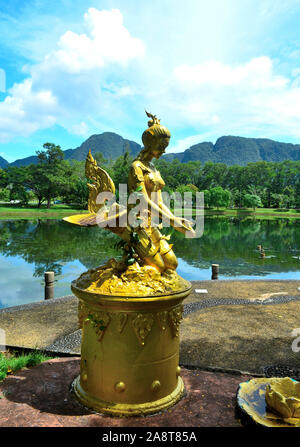 Eine goldene Statue einer Frau vor dem See spiegelnde Landschaft in Somdet Phra Srinagarinda Park mit Bergketten im Hintergrund zu beten. Stockfoto