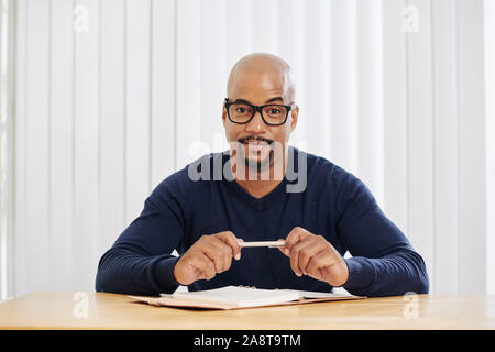 Positive glatzköpfige Mann mit Kreis Bart am Schreibtisch sitzen und sich Notizen in Planer Stockfoto