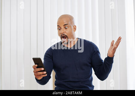 Schockiert Mann mit großen Augen öffnen den Mund beim Lesen von SMS auf dem Smartphone Stockfoto