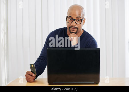Portrait von Stattlichen positive Mixed-race Mann bezahlen mit Kreditkarte für Online Einkäufe Stockfoto