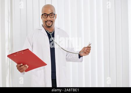 Positive lächelnde Arzt für Allgemeinmedizin mit medizinische Geschichte und Stethoskop in den Händen Stockfoto