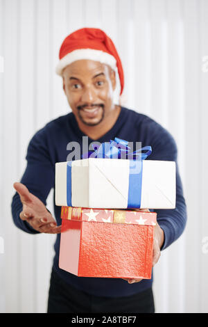Weihnachtsgeschenke in den Händen von lächelnden Mann in Santa Hut, selektiver Fokus Stockfoto