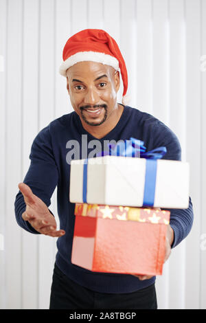 Positive mixed-race Mann in Santa Claus hat Holding Weihnachtsgeschenke für Freunde und Verwandte Stockfoto