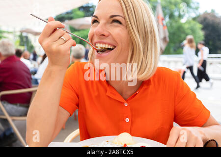 Junge Frau sitzt in einem Cafe in Wien und frisst Österreichs traditionelle süße Apfelstrudel mit Sahne und Vanilleeis, Wien, Österreich Stockfoto