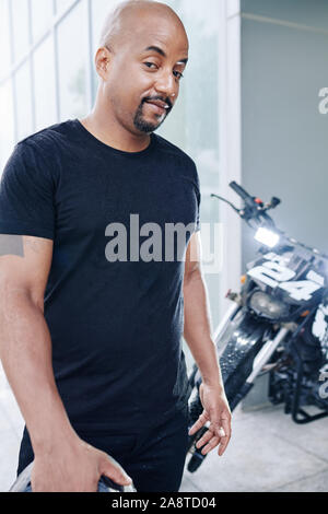 Portrait von stattlichen Motorradfahrer mit Kreis Bart stehen in einer Garage. Stockfoto
