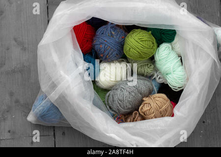 Kugeln aus Wolle Garn in einer Auswahl von Farben und Stile in einer weißen Tasche. Holzboden Hintergrund durch selektive Farbkorrektur Stockfoto