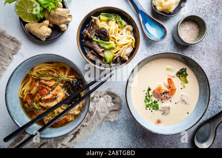 Satz serviert asiatische Suppen auf grauem Hintergrund der Ansicht von oben. Tom Yum Suppe, Aal Fischsuppe und Ramen Noodle Soup Stockfoto