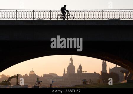 Dresden, Deutschland. 11 Nov, 2019. Bei Sonnenaufgang, ein Radfahrer kreuzt die Marienbrücke Brücke vor der Kulisse der Altstadt und zeichnet sich als Silhouette. Credit: Sebastian Kahnert/dpa-Zentralbild/dpa/Alamy leben Nachrichten Stockfoto