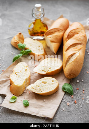 In Scheiben geschnittene Frische knusprigem Baguette mit Salz, Olivenöl und Basilikum auf einem grauen konkreten Hintergrund Stockfoto