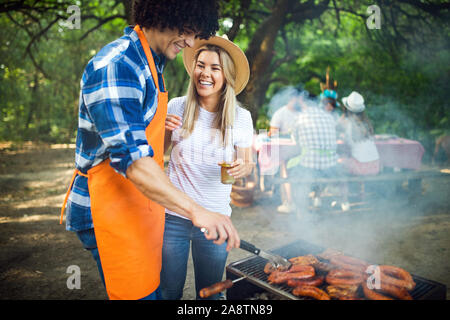 Junges Paar Vorbereitung Würstchen auf den Grill im Freien Stockfoto