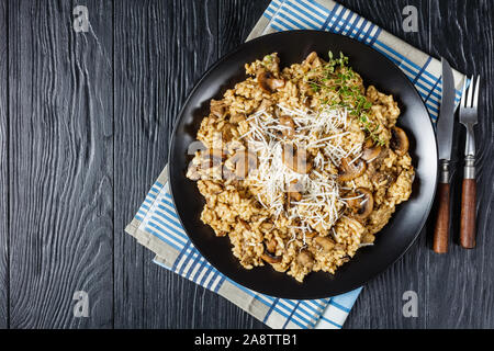 Steinpilzen cremige Risotto mit geriebenem Käse und Thymian auf schwarzem Teller auf einem Holztisch, Ansicht von oben, flatlay, freier Speicherplatz Stockfoto