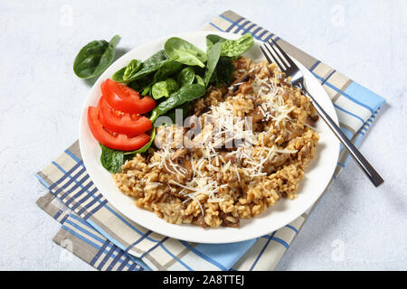 Steinpilzen cremige Risotto mit geriebenem Käse und Spinat tomaten salat auf einem weissen Teller, horizontale Ansicht von oben. close-up Stockfoto