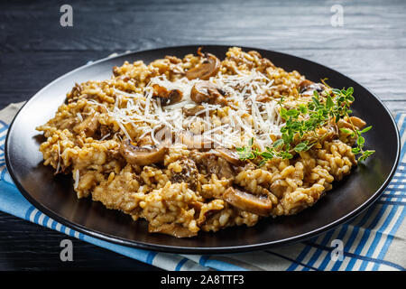 In der Nähe von Pilzen cremige Risotto mit geriebenem Käse und Thymian auf eine schwarze Platte mit Zutaten auf einem Holztisch, horizontale Ansicht von oben Stockfoto