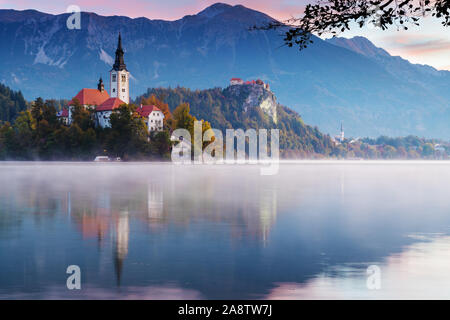 Schönen Morgen am Bleder See bei Sonnenaufgang. Nebel verweilend über den See mit der katholischen Kirche auf der Insel und das alte Schloss mit Bergen im Hintergrund Stockfoto