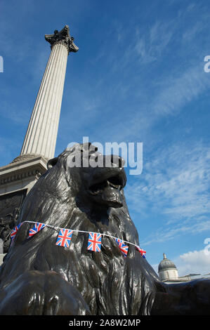 Blick auf den von Trafalgar Square aus dem Jahr 1867 installierten Löwen mit der Flagge des British Union Jack, die sich am Fuß der Nelsonsäule in London, Großbritannien, befindet Stockfoto