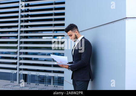 Junge Unternehmer Asiaten hält und hält, liest und sortiert Papiere, steht in der Nähe der Wand des Business Center. Stockfoto