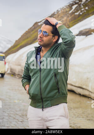 Close up Portrait Of Happy indischen Mann mit Winterjacke und Sonnenbrille, in Leh, Ladakh Region stehen im Winter. Berge und Schnee Hintergrund. Stockfoto