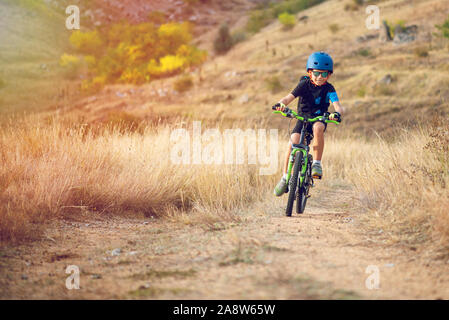 Glückliches Kind Junge von 7 Jahren Spaß im Herbst Park mit dem Fahrrad auf schönen Herbst Tag. Aktives kind Fahrradhelm tragen Stockfoto