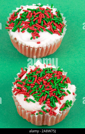 Zwei selbstgemachte Red velvet Weihnachtsferien cupcakes gekrönt mit einem Frischkäse weiße Zuckerglasur mit Urlaub in den Farben rot grün und Weiß besprüht. Stockfoto