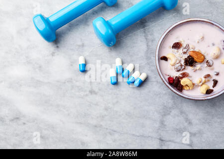 Sport Ergänzungen auf Stein. Schüssel Müsli mit Joghurt, Nüssen, Rosinen, Preiselbeeren und Chia Samen und blau Hanteln in Hintergrund. Stockfoto