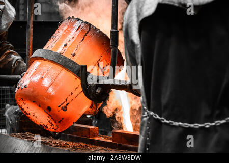 In einer Gießerei-Werkstatt. Das geschmolzene Metall wird in eine Form aus einem Tiegel ausgegossen durch zwei Arbeiter manövriert Stockfoto