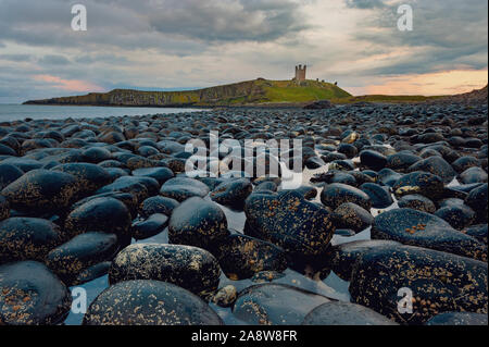 Dunstanburgh Castle aus den Steinen am Ufer des Embleton Bucht an der Küste von Northumberland. Stockfoto