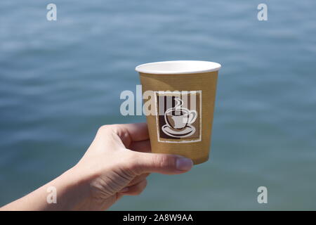 Malta, Mai 2019: Women's Hand papercup mit Kaffee vor der Wellen des Ozeans. Übersicht Recycling und Abfall. Stockfoto