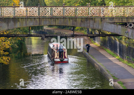 Kanal lastkahn vorbei unter einer Brücke an der Regent's Canal Vergangenheit London Zoo mit einem Läufer auf der Zehe Pfad Stockfoto