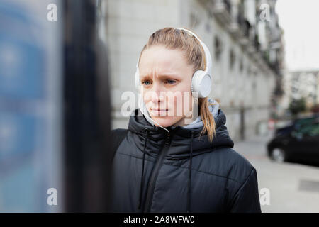 Junge blonde Frau Zahlung auf die parkuhr in der Stadt mit überraschten Gesicht trägt eine Jacke ein Kopfhörer Stockfoto