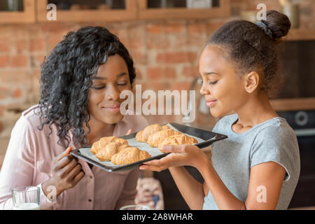 Fröhliches kleines Mädchen riechen selbstgemachte Croissants mit Mom Stockfoto