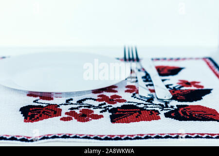 Tabelle Einstellung für Abendessen: Ein weißer Teller, Gabel, ein Messer auf einem gewebtem Stoff Serviette mit gesticktem Muster, traditionelle Handarbeit in der Ukraine Stockfoto