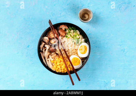 Ramen. Soba Nudeln mit gekochten Eiern, Shiitake-pilze, und Gemüse, geschossen von oben auf blauem Hintergrund mit Stäbchen, Sake und Kopie Raum Stockfoto