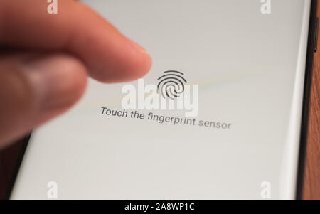 male hand holding mobile phone showing application with process of scanning fingerprint on a screen Stockfoto