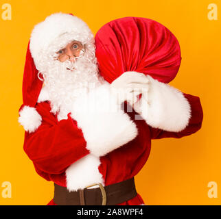 Santa Claus mit großen roten Sack auf seinem Rücken auf Orange Stockfoto