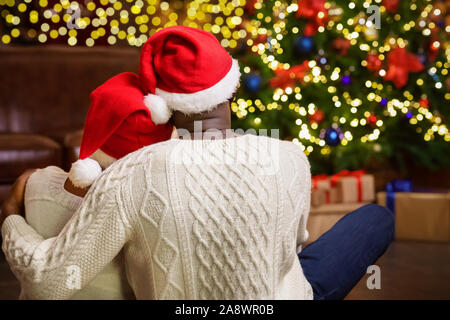 Schwarz Paar in Santa Hüte sitzen in der Nähe von Weihnachten Baum Stockfoto