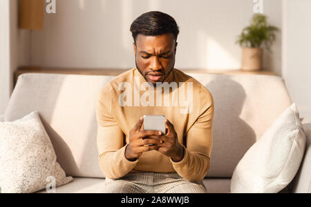 Man SMS am Telefon die Stirn runzelnd Sitzen auf der Couch zu Hause Stockfoto