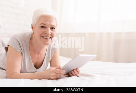 Lächelnde ältere Frau im Bett liegend und Vernetzung im digitalen Tablet Stockfoto