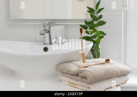 Zwei braune biologisch abbaubaren, kompostierbaren Bambus Zahnbürsten auf einem Handtuch im Bad weißer Innenausstattung. Grüne Pflanze Dekor in den Hintergrund. Stockfoto