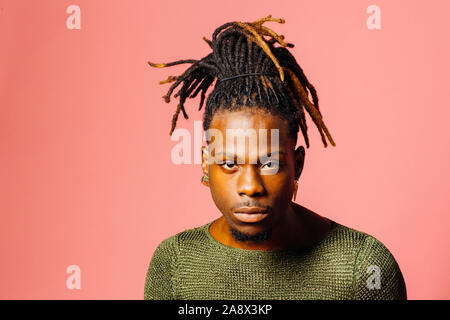 Porträt einer ernsthaften jungen Mann mit Dreadlocks Frisur bei Camera suchen, isoliert auf Rosa Stockfoto