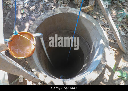Luftbild von der Tiefe eines Brunnens. Tiefe der konkreten Ringe mit blauen Seil und orange Eimer mit Wasser gefüllt. In der tiefen, Licht reflektiert. Stockfoto