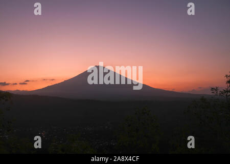 Hellen Himmel in Rot und Orange, kurz nach Sonnenuntergang. Die Sonne hinter den Agung Vulkan auf Bali Insel und ein silet des Berges Stockfoto