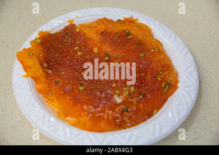 Eine Scheibe des Kanafeh, einer traditionellen nahöstlichen leckeres Dessert, in einem weißen Teller serviert Stockfoto