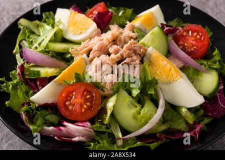 Salat mit Thunfisch, Ei und Gemüse auf schwarz und grau hinterlegt. Nahaufnahme Stockfoto