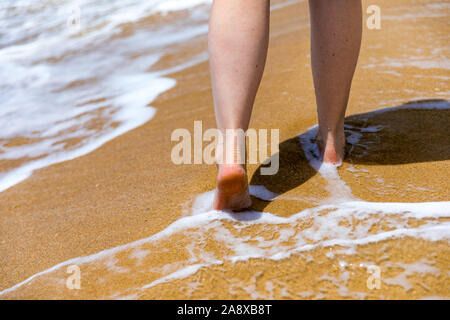 Frau barfuß am Strand. Close up Bein der jungen Frau zu Fuß entlang der Welle von Meer Wasser und Sand auf dem Sommer Strand. Travel Concept. Frau Wal Stockfoto