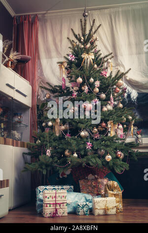 Es ist die Heilige Nacht, die geschmückten Weihnachtsbaum im Wohnzimmer und unten sind die aufgewickelte Weihnachtsgeschenke. Authentisches Bild der eigenen Partei. Stockfoto