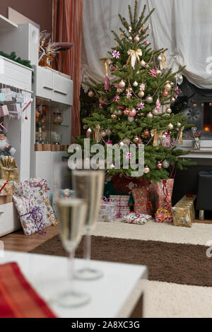 Es ist die Heilige Nacht, die geschmückten Weihnachtsbaum im Wohnzimmer und unten sind die aufgewickelte Weihnachtsgeschenke. 2 Gläser Sekt sind in Stockfoto