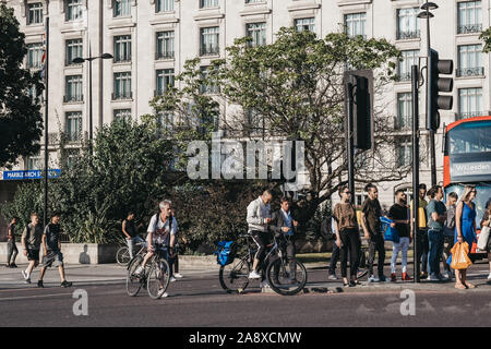 London, Großbritannien - 18 Juli 2019: Fußgänger und Radfahrer auf der Straße neben dem Marble Arch, London, ein Gebiet Namen, die nach dem 9. Jahrhundert weiß marbl zu überqueren Stockfoto